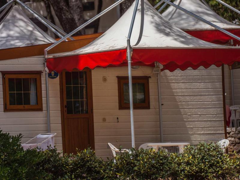 Drewniana chatka z czerwonym daszkiem i zielonymi roślinami z przodu w miejscu urlopowym.