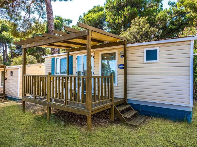 Dom mobilny z werandą i zielonym trawnikiem w zalesionym otoczeniu