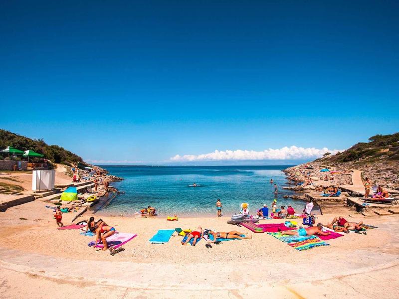 Mała piaszczysta plaża między skałami z ludźmi i czystą niebieską wodą pod niebieskim niebem.