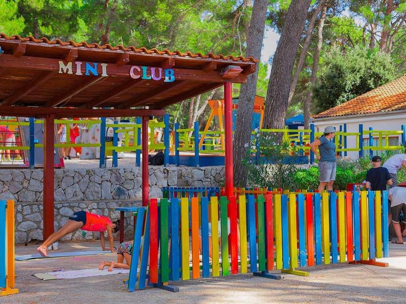 Kolorowy plac zabaw dla dzieci z budką mini klubu i kilkorgiem dzieci na zewnątrz.