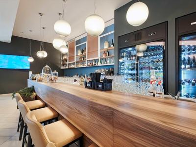 Moderner Barbereich mit Holztheke, bequemen Hockern und beleuchteten Getränkeregalen.