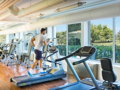 Moderne Fitnessstudio mit großen Fenstern und Blick auf grüne Bäume.