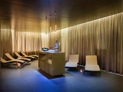 Moderner Wellnessraum mit Ruheliegen, sanfter Beleuchtung und Vorhängen aus cremefarbenem Stoff.