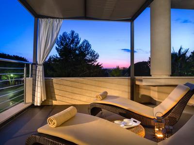 Gemütliche Terrasse mit Liegestuhl, weißen Vorhängen und Abendhimmel mit Bäumen im Hintergrund.