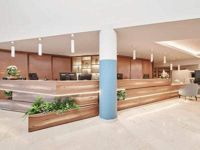 Moderne Rezeption mit hellen Holzflächen, grünen Pflanzen und weißen Pendelleuchten.