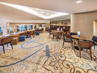 Großer moderner Hotel-Loungebereich mit Teppichboden, gemütlichen Stühlen und warmem Licht.