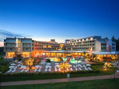 Modernes Hotel bei Dämmerung mit beleuchtetem Pool und Außenbereich mit Liegestühlen.