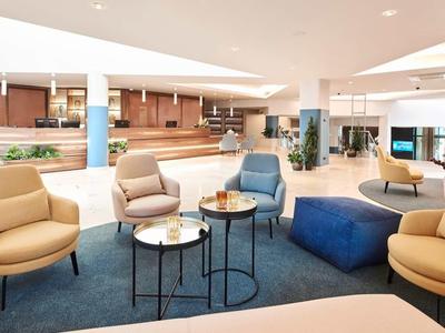 Großer, heller Raum mit modernen Sofa- und Sesselmöbeln in Beige und Blau, runden Tischen und Teppich.