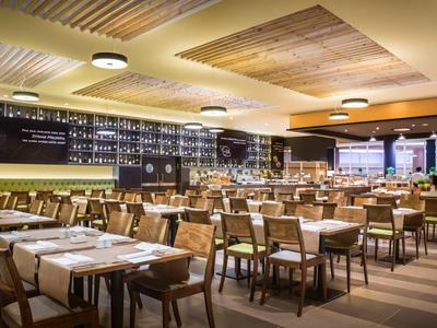 Modernes Restaurant mit Holzmöbeln, gedeckten Tischen und einer langen Bar mit Beleuchtung.