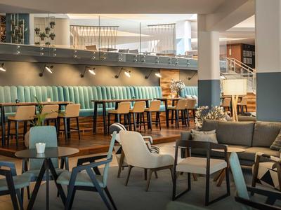 Moderne Caféecke mit Holzstühlen, blauen Polstern und gemütlichen Sesseln in warmem Licht.