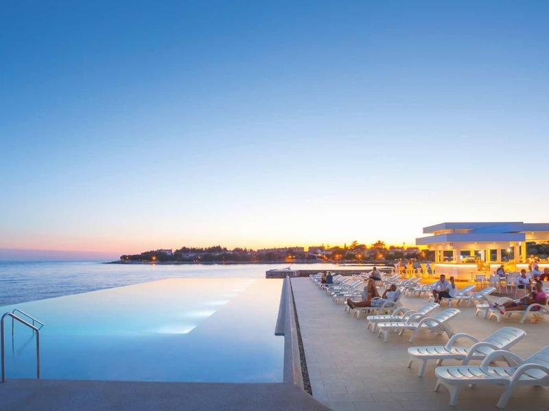 Infinity-Pool am Meer bei Sonnenuntergang mit Liegestühlen und klarem Himmel.