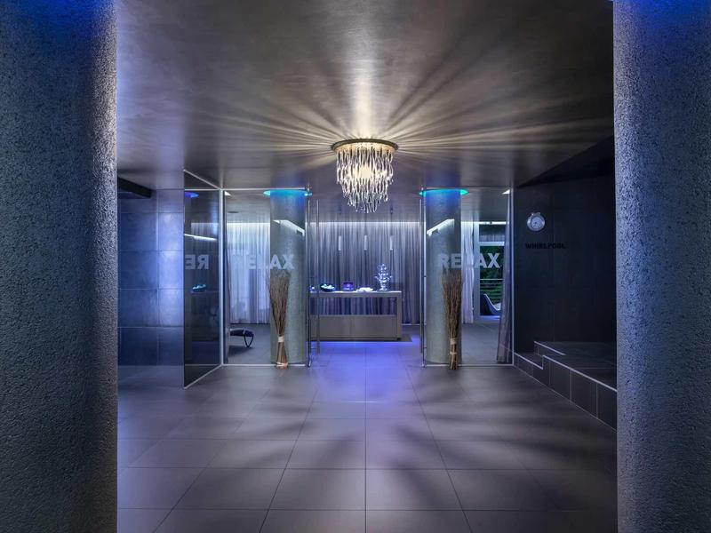 Moderner Eingangsbereich mit silbernen Säulen, blauem Licht und funkelndem Kronleuchter.