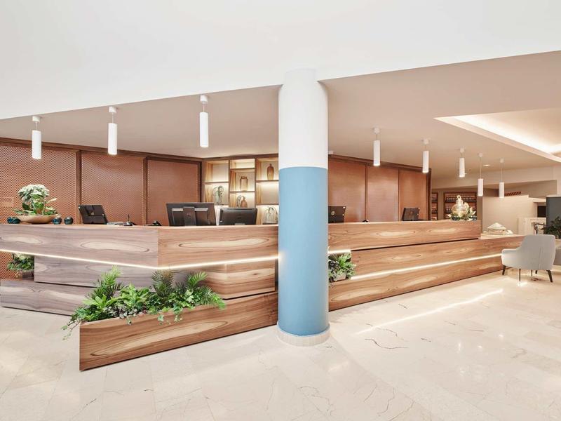 Moderne Rezeption mit hellen Holzflächen, grünen Pflanzen und weißen Pendelleuchten.