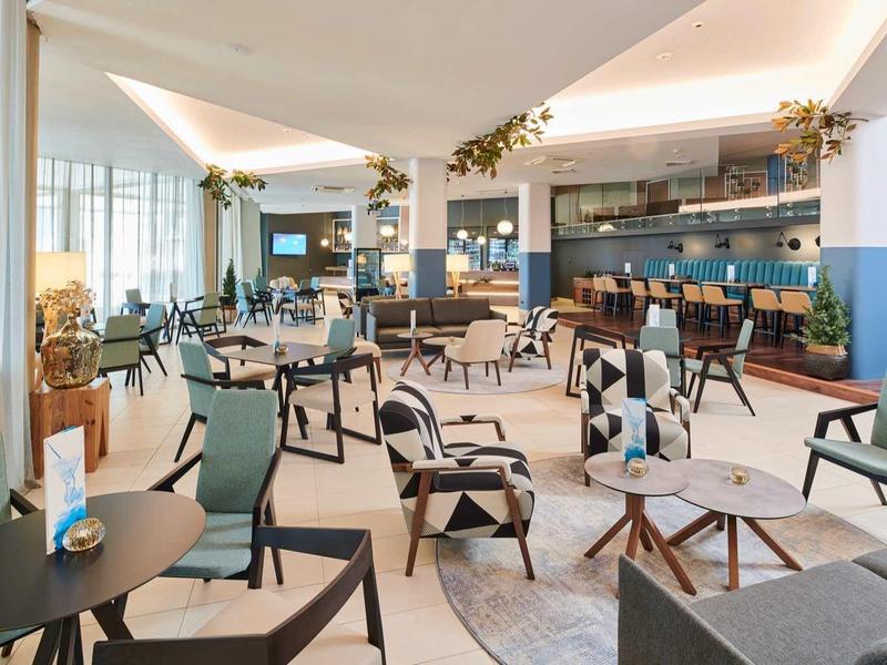 Großer, heller Gastraum mit modernen Stühlen, Tischen und großer Fensterfront im Tageslicht.