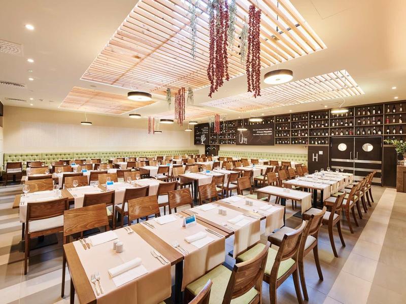 Modernes Restaurant mit Holzstühlen, langen Tischen und schattierten Deckenlampen.