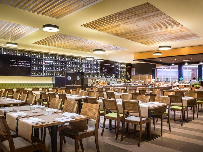 Modernes, helles Restaurant mit Holztischen, bequemen Stühlen und gemütlicher Deckenbeleuchtung.