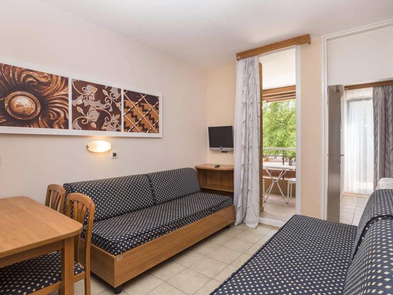 Mały pokój hotelowy z dwoma rozkładanymi sofami, drewnianymi meblami i dostępem do balkonu.