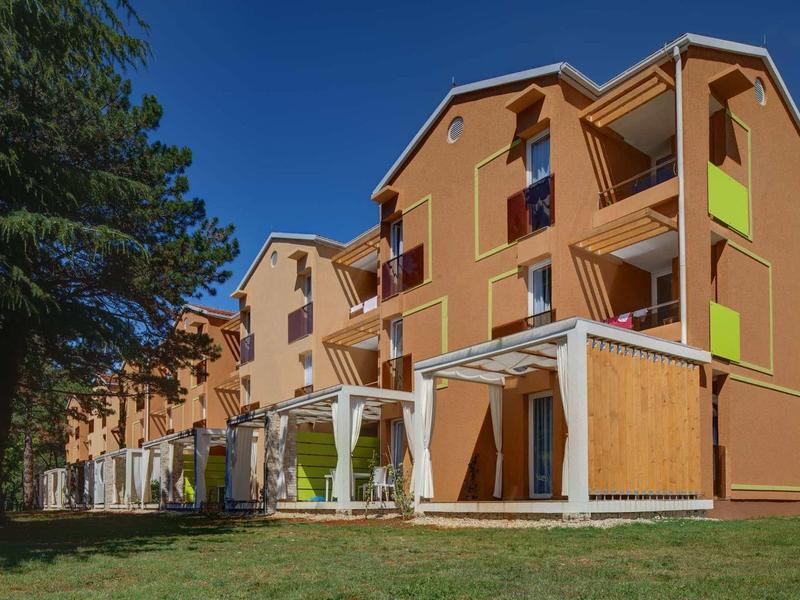 Wielopiętrowy brązowy budynek mieszkalny z balkonami i zielonym trawnikiem z przodu