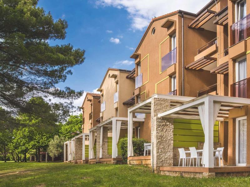 Wielopiętrowy hotel z tarasami i ogrodem pod niebieskim niebem w spokojnej okolicy.