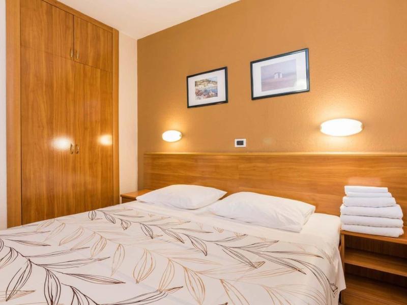 Przytulne łóżko dwuosobowe z wzorzystą pościelą, stolikiem nocnym i dekoracjami na ścianie w ciepłych tonach.