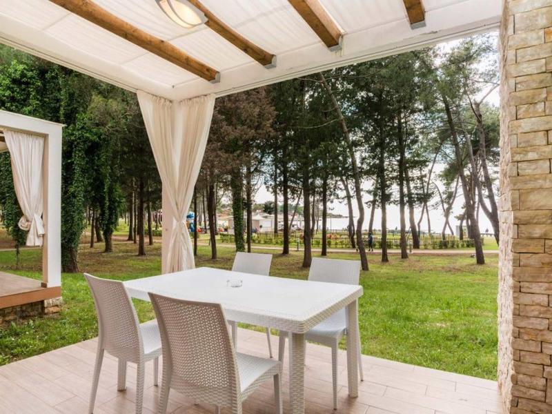 Taras z stołem jadalnym i krzesłami z widokiem na zalesiony ogród.