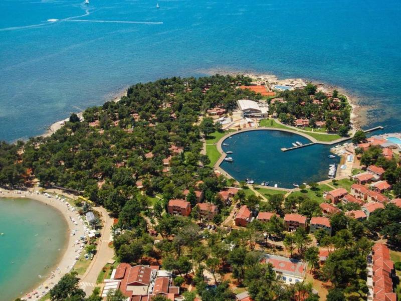 Ośrodek na wyspie z basenem, otoczony drzewami i morzem.