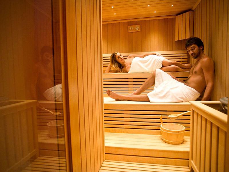 Zwei Personen entspannen in einer hölzernen Sauna, eine sitzt, die andere liegt entspannt.