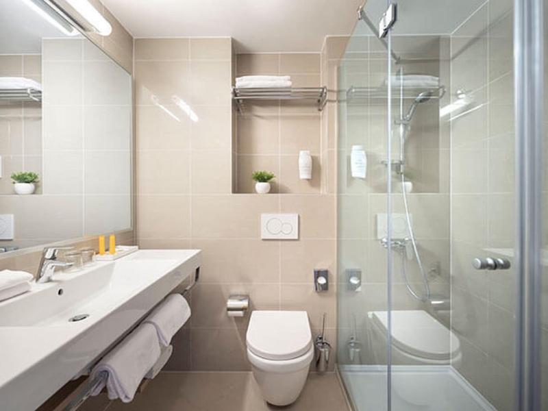 Modernes Badezimmer mit weißer Toilette, großem Spiegel, Waschbecken und Duschkabine aus Glas.