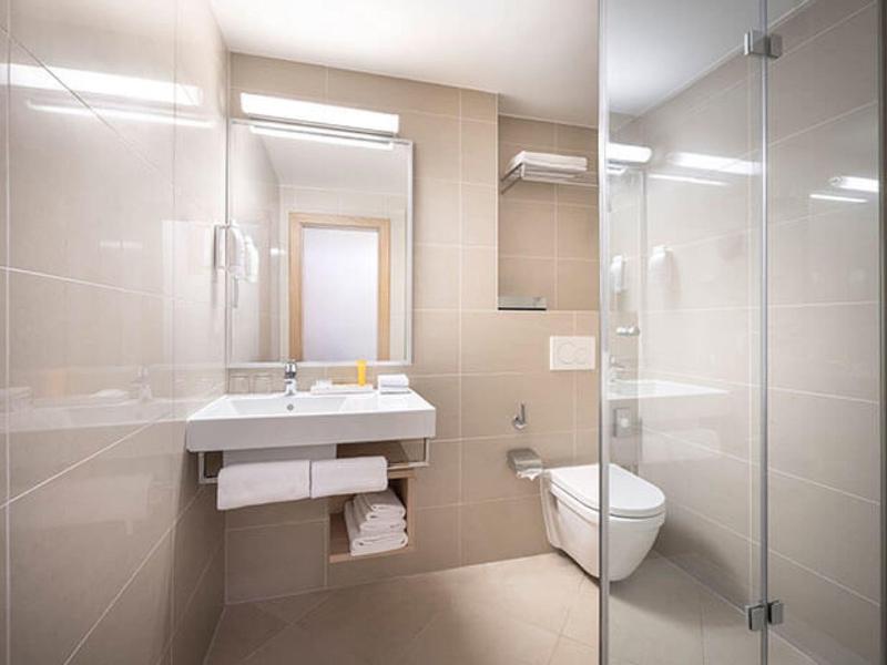 Kompaktes, modernes Badezimmer mit weißem Waschbecken, Spiegel, WC und Glasdusche.