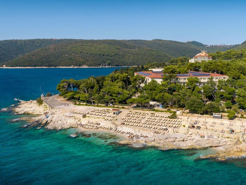 Küstenblick auf ein Hotel mit Strandliegen und blauem Meer an einem sonnigen Tag.