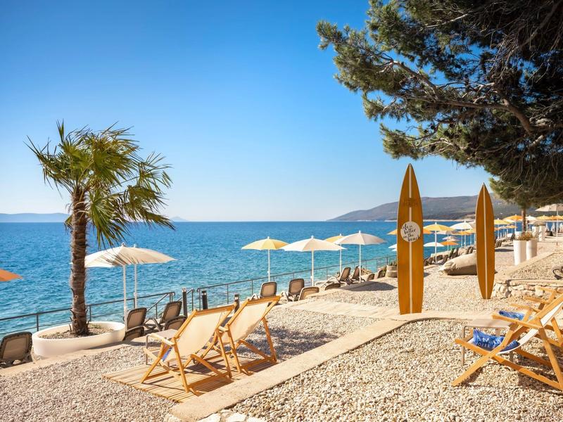 Strand mit Liegestühlen, Sonnenschirmen und Surfbrettern bei klarem Himmel.