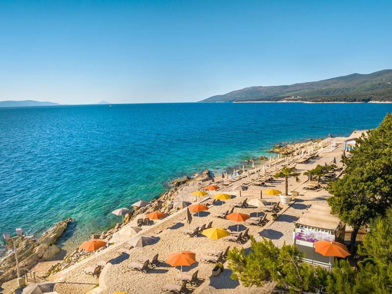 Strand mit Sonnenschirmen und klarem blauem Meer an einem sonnigen Tag.