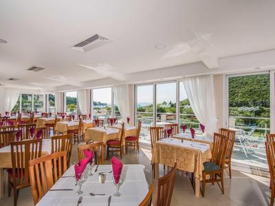 Helles Restaurant mit Holztischen, Stühlen und Blick auf grüne Landschaft durch große Fenster.
