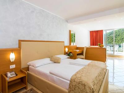 Hell dekoriertes Hotelzimmer mit einem Doppelbett, Nachttisch, Arbeitsbereich und Zugang zum Balkon.