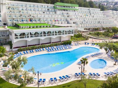 Großes Hotel mit mehreren Pools, grünen Sonnenschirmen und Liegestühlen an einem sonnigen Tag.