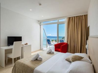Hotelzimmer mit Doppelbett, Schreibtisch, Stühlen und Blick auf das Meer durch große Fenster.