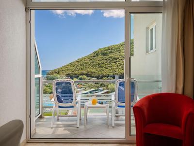 Blick von einem Hotelzimmer auf Balkon mit zwei Stühlen und grünem Hügel im Hintergrund.