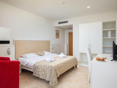 Helles, schlicht eingerichtetes Hotelzimmer mit Doppelbett, rotem Sessel und Schreibtisch.