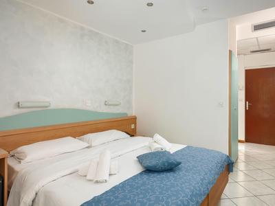 Ein schlicht eingerichtetes Hotelzimmer mit Doppelbett, blauer Tagesdecke und weißen Wänden.