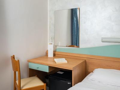 Ein schlichter Hotelzimmer-Schreibtisch mit Holzstuhl, Spiegel und kleiner Minibar unter dem Tisch.
