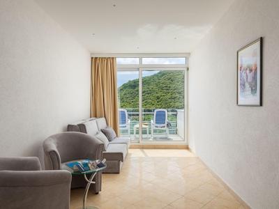 Heller Zimmerbereich mit grau gepolsterten Stühlen, Sofa und Balkon mit Blick auf grüne Hügel.