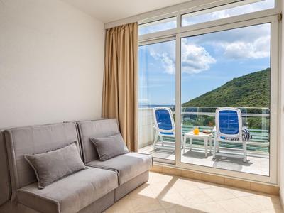 Helles Zimmer mit grauem Sofa und Balkon mit Meerblick und zwei blauen Stühlen.