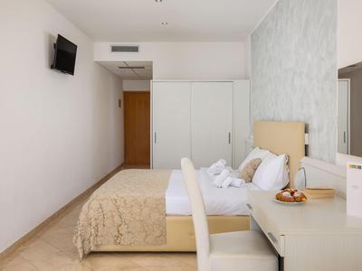 Hell eingerichtetes Hotelzimmer mit Doppelbett, Schrank, Schreibtisch und Wandfernseher.