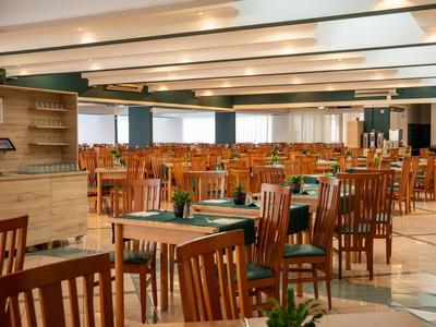 Geräumiger Hotel-Speiseraum mit Holztischen und Stühlen, heller Beleuchtung und gepflegtem Ambiente.