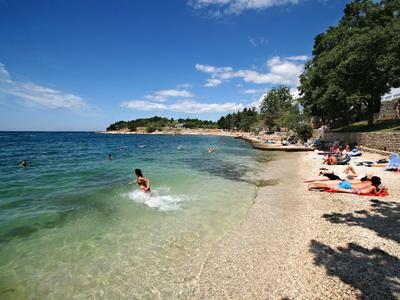 Strand mit klarem Wasser, Menschen im Wasser und auf der sandigen Uferpromenade unter blauem Himmel