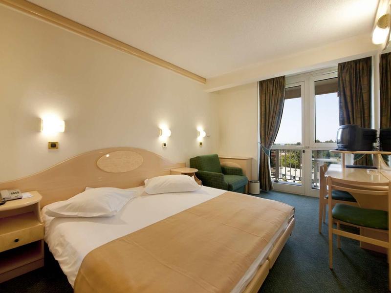 Gemütliches Hotelzimmer mit Doppelbett, Nachttischen, grünem Sofa, Schreibtisch und Balkonblick.