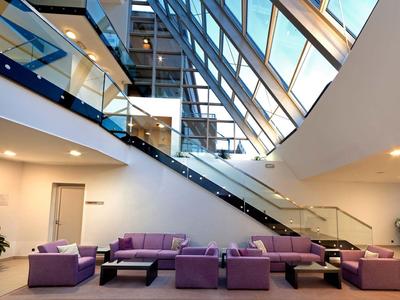 Moderne Hotellobby mit purpurfarbenen Sofas und Glasaufzug unter einem Glasdach.