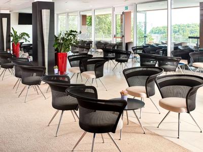 Moderne Lounge mit schwarzen Stühlen und Tischen in einem hellen Raum mit großen Fenstern.
