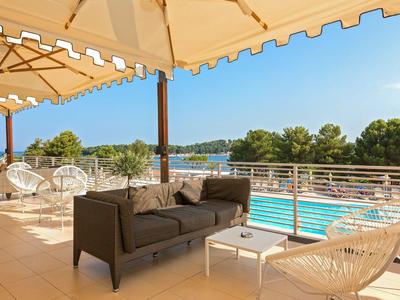 Terrasse mit Sitzgelegenheiten und Blick auf einen Pool und grüne Landschaft unter blauem Himmel.