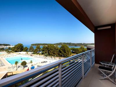 Balcone con vista su una piscina e un paesaggio verde sotto un cielo terso.